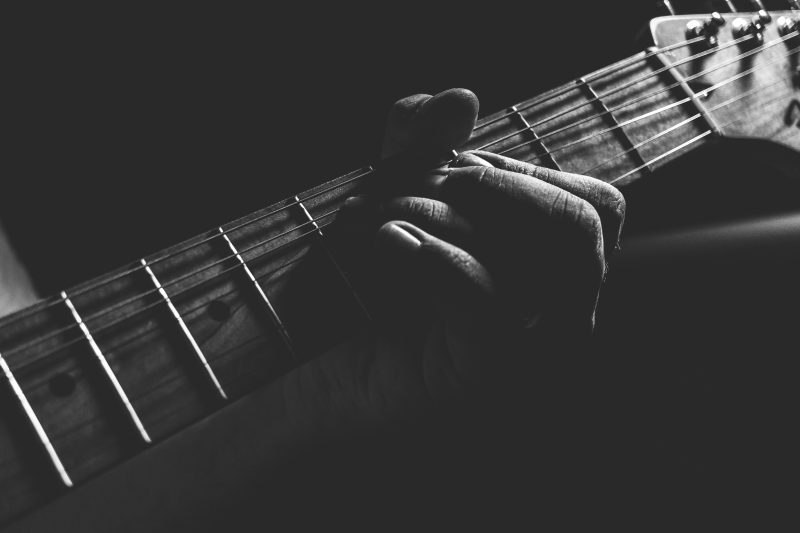 Black and white image of hand on guitar strings