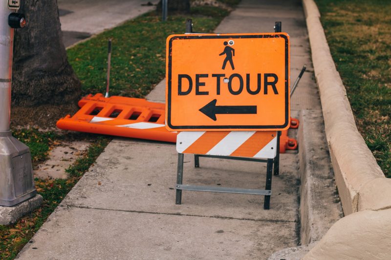 orange detour sign on sidewalk, with arrow to the left